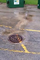 drain in parking lot with runoff coming from garbage container