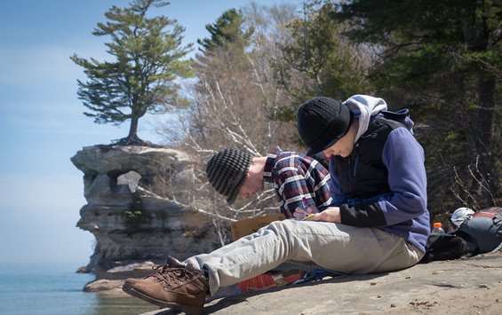 Two students sitting on a large rock by the water