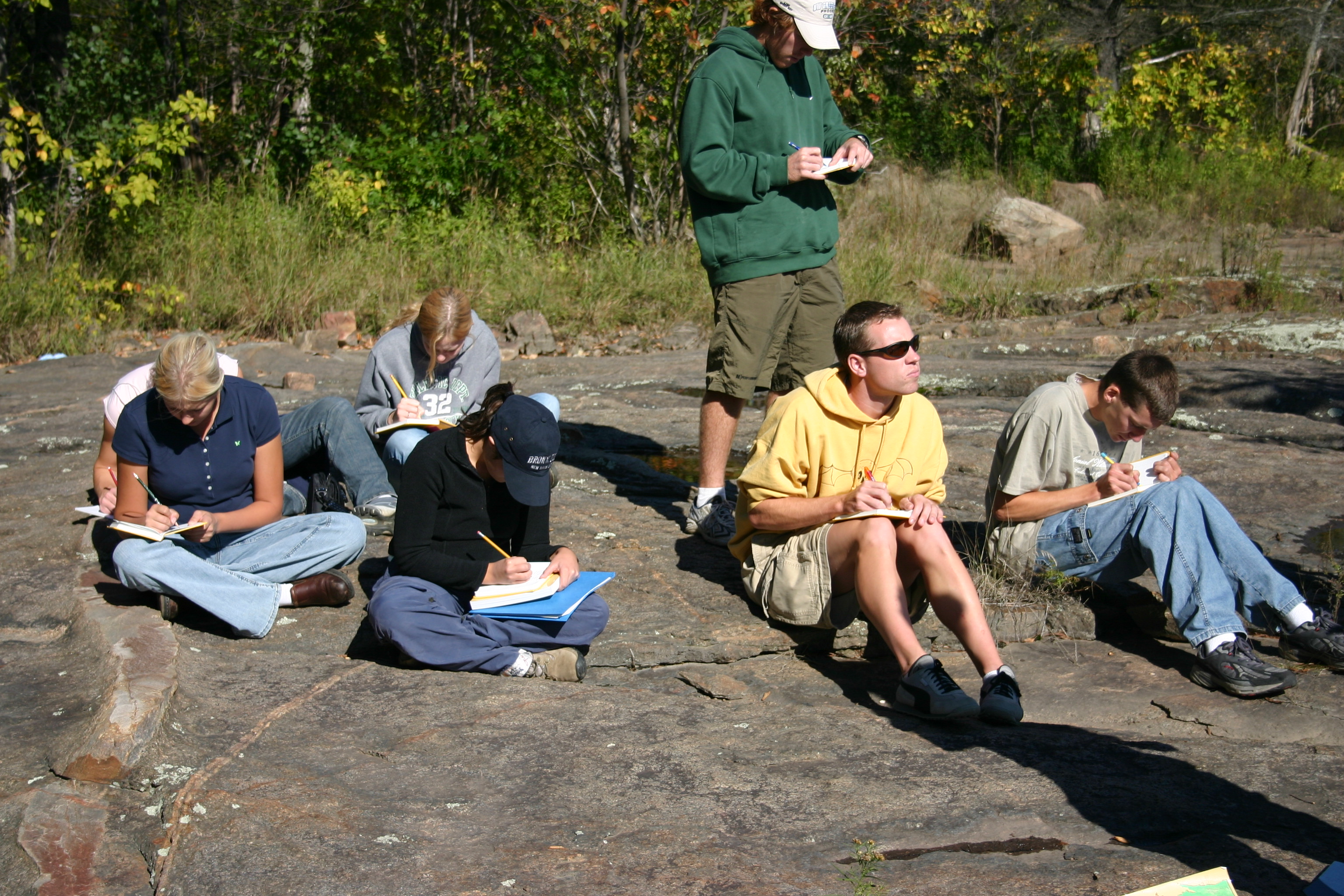 Two students sitting on a large rock by the water