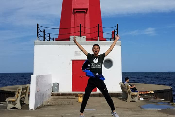 A UWGB, Marinette Campus student jumps near a lighthouse.