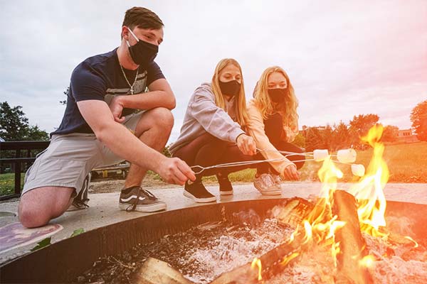 Students wearing masks, making s'mores at the fire pit