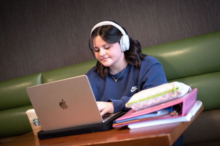 Female student wearing headphones studies on laptop