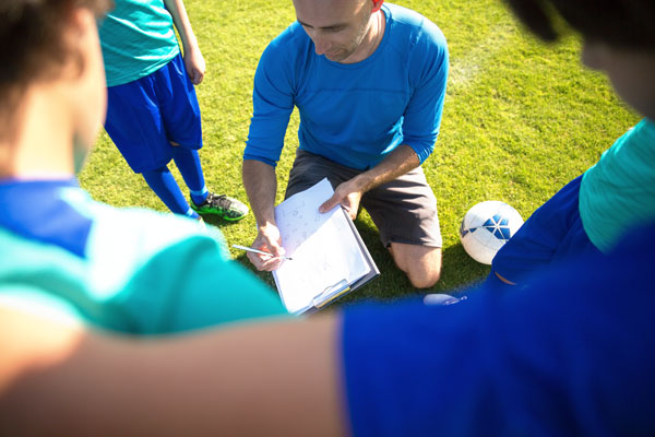 Coach kneeling down while going over plays with soccer team