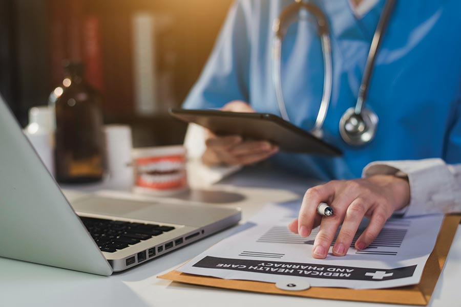 A nurse at their desk with a notepad, pen, and laptop.