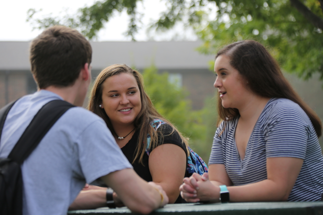 three students talking at a table outdoors