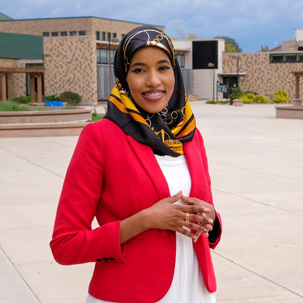UW-Green Bay student Naima Musse, wearing a hijab and red blazer standing on the student services plaza