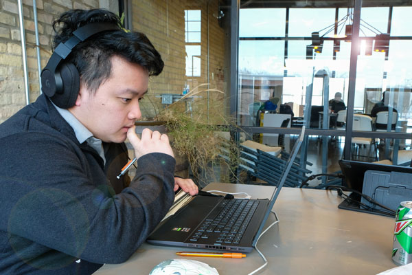 Asian male student wears headphones and studies at computer