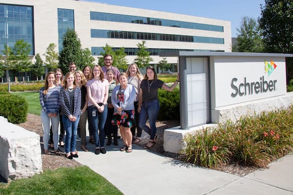 Group of Schreiber interns pose next to Schreiber sign