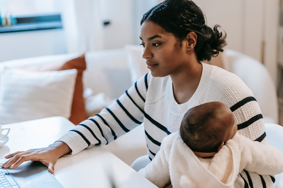 Young mother working on a laptop while holding an infant