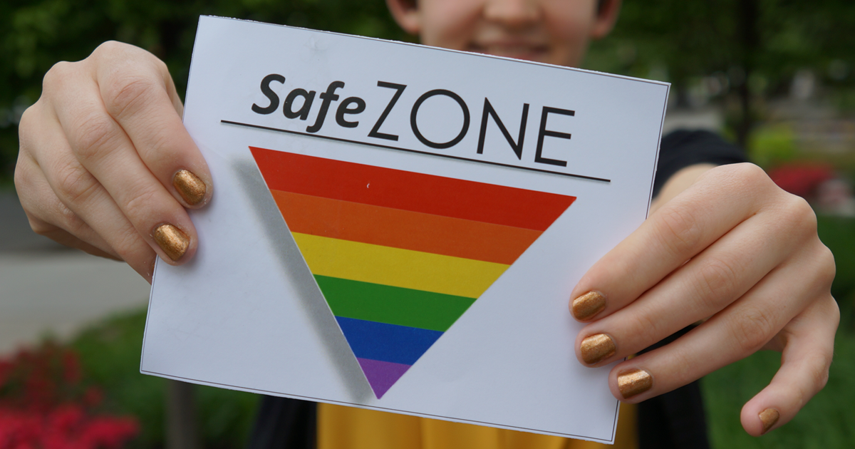 Person holding a card that says Safe Zone with a rainbow triangle