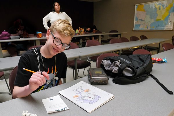 A Pride Center camp participants sits at a desk and sketches during an arts and crafts project
