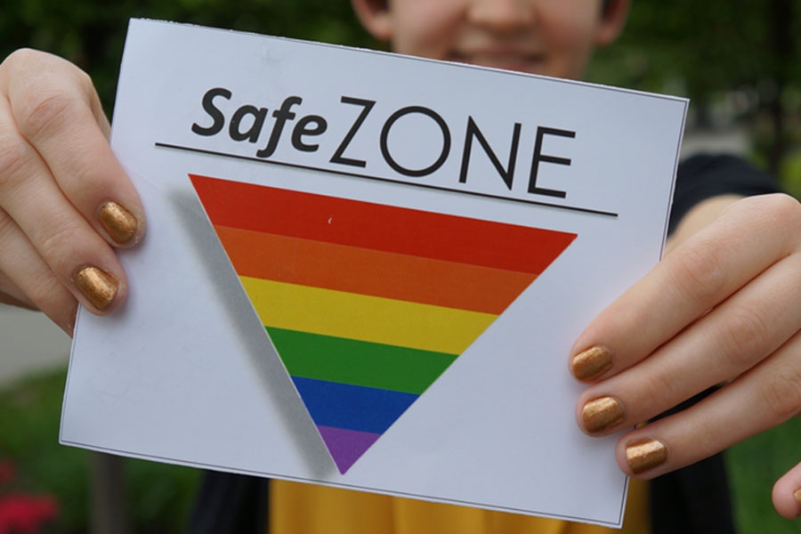 Student proudly displaying a sign featuring pride colors that says "safe zone