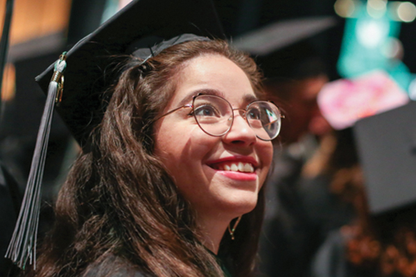 A woman smiling while wearing a graduation cap and gown.