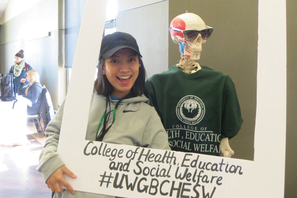 Student posing while holding College of Health Education and Social Welfare sign