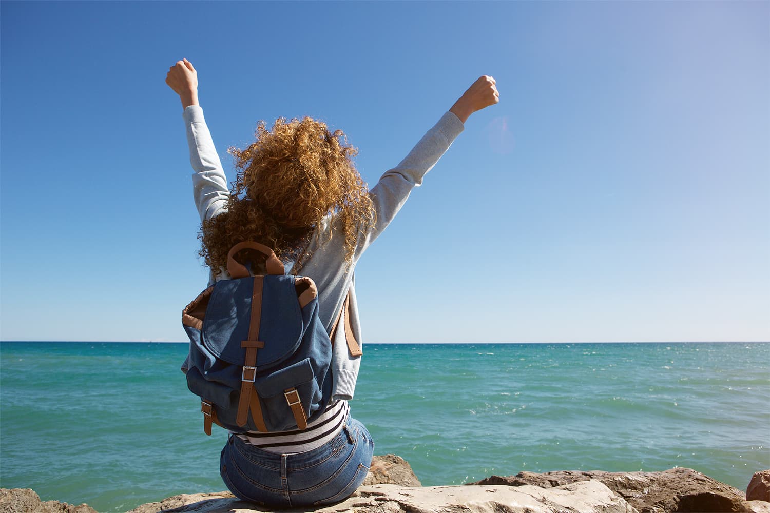 Rising Phoenix student sitting on the shore with arms raised