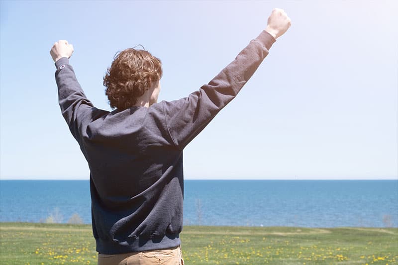 Student with arms up outside by Lake Michigan