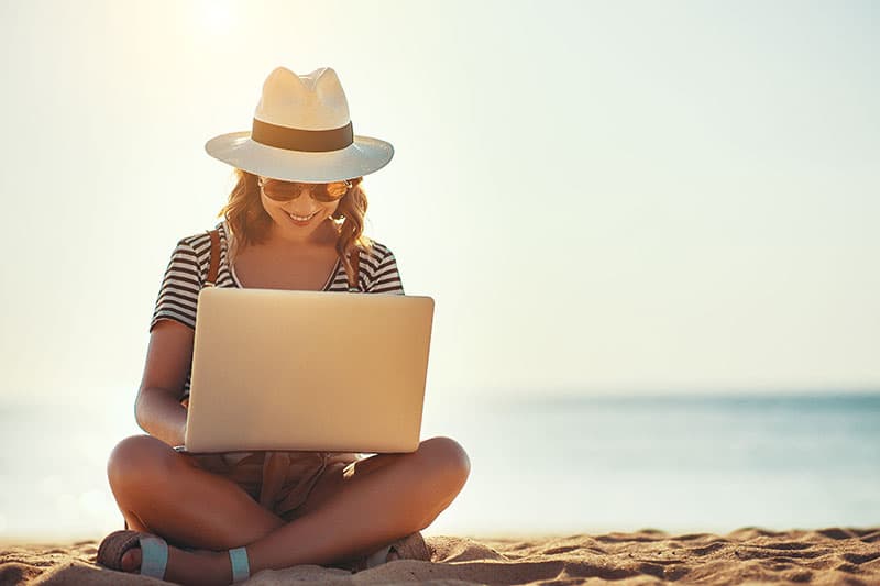 Young woman working on laptop outside at beach
