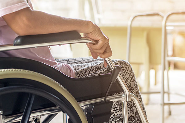 Senior person seated in a wheelchair with a walker in the distance