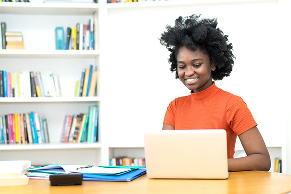 Young black woman happily typing up her résumé on a laptop