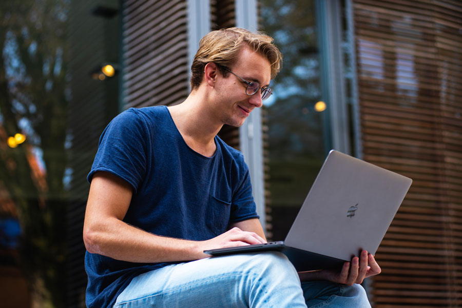 Male student sitting outside while attending online class