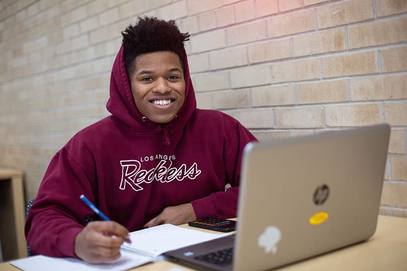 student smiling looking up from laptop while studying