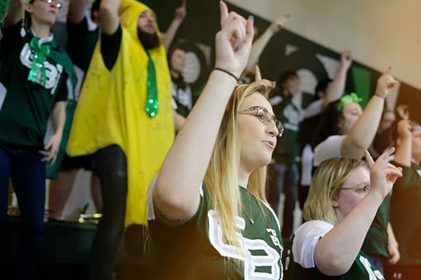 student wearing GB shirt cheering at basketball game