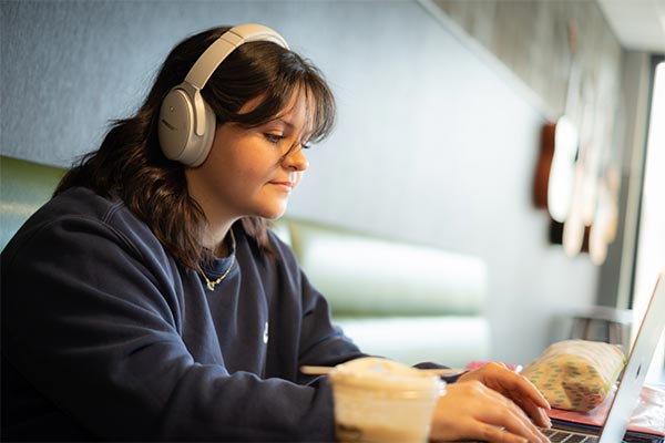 UWGB student wearing headphones and using a laptop in the Common Grounds coffee shop