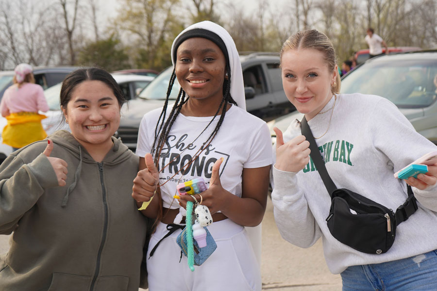 Three students signal thumbs up and smile for photo