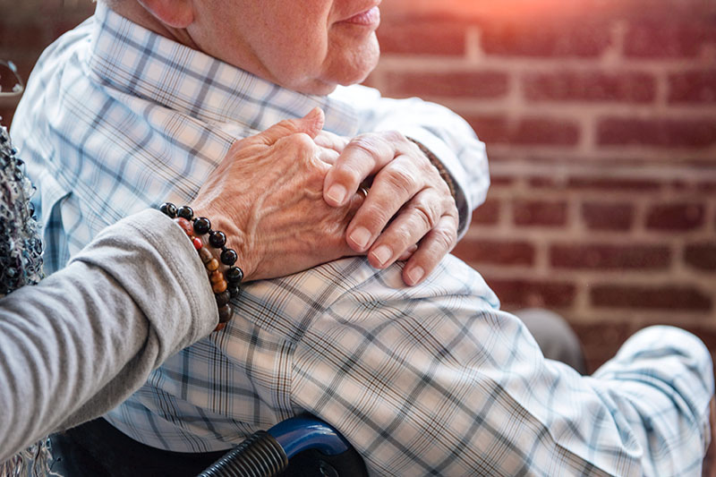 Elderly man in wheelchair holding wifes hand