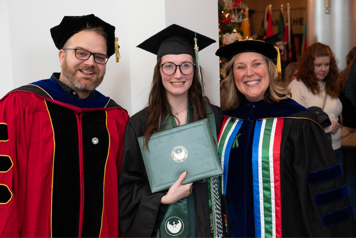 Two faculty members pose with a student and their diploma after commencement