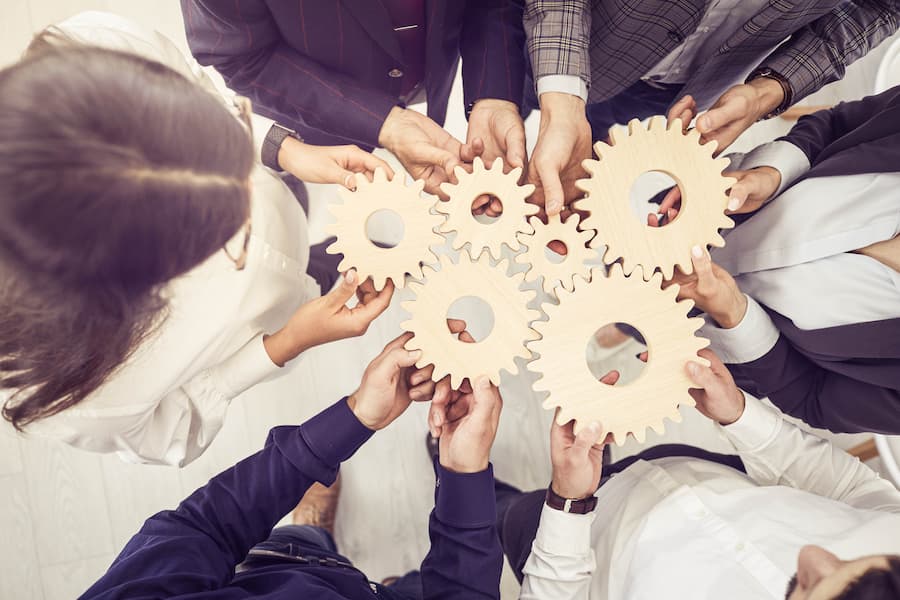 Group of employees hold together wooden gears signifying teamwork