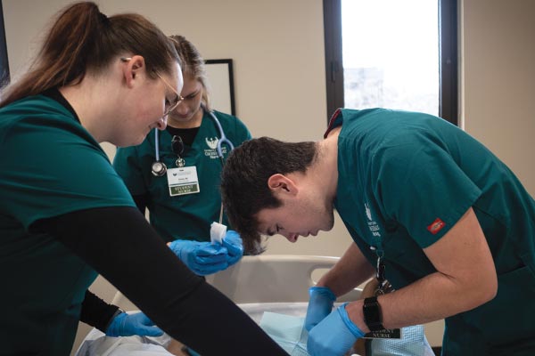 Three nursing students practice a check-up using a dummy