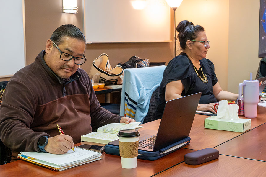 First Nations students taking notes and working on laptop in class.