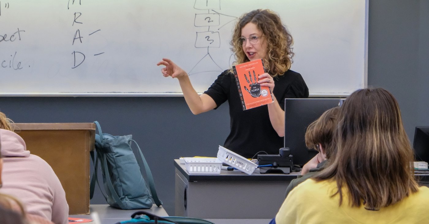 instructor in front of class holding book
