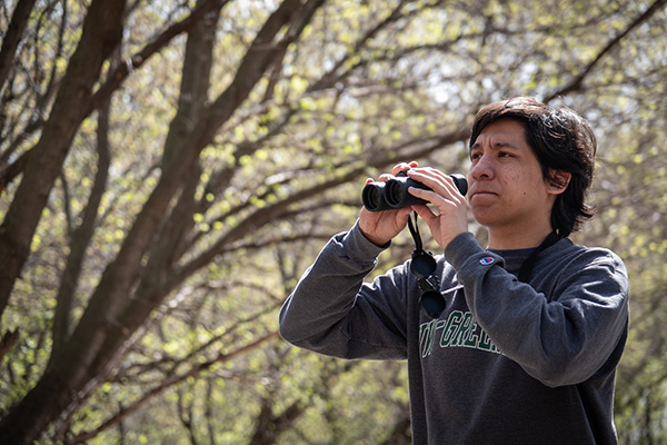 Young man with binoculars around trees