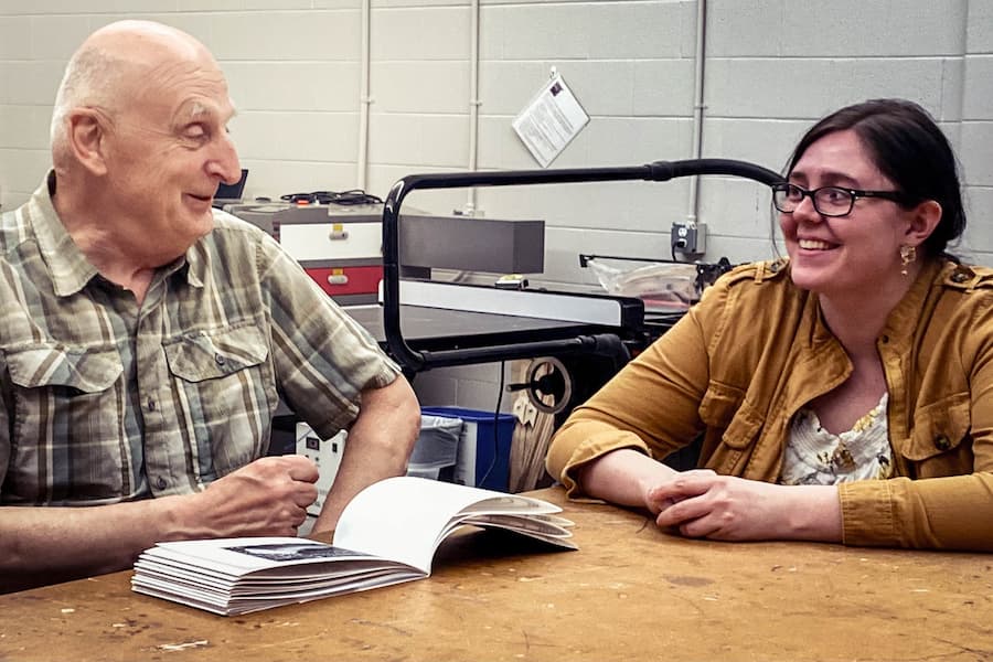 Writing and applied arts intern works with older gentleman at desk
