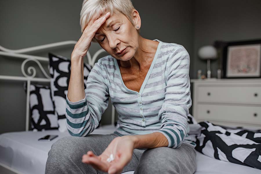 senior woman sitting on bed with pills in hand