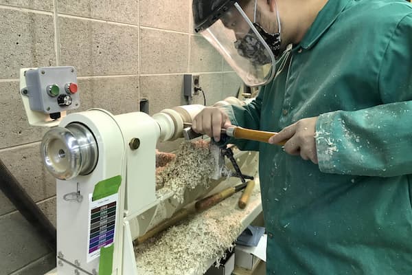 Student carves table leg in wood shop studio