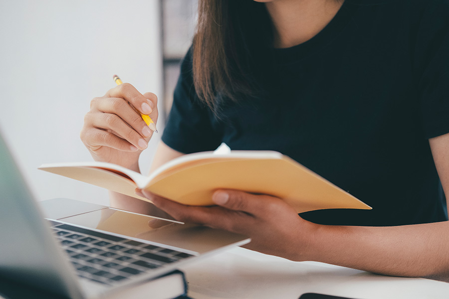 Girl at laptop with notebook in hand