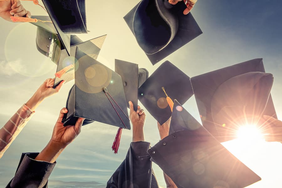 Students raise graduation hats in celebration.