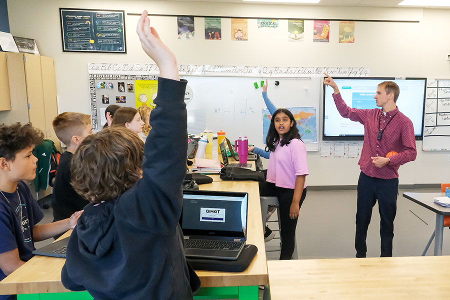 Teacher in classroom with young students raising their hands.