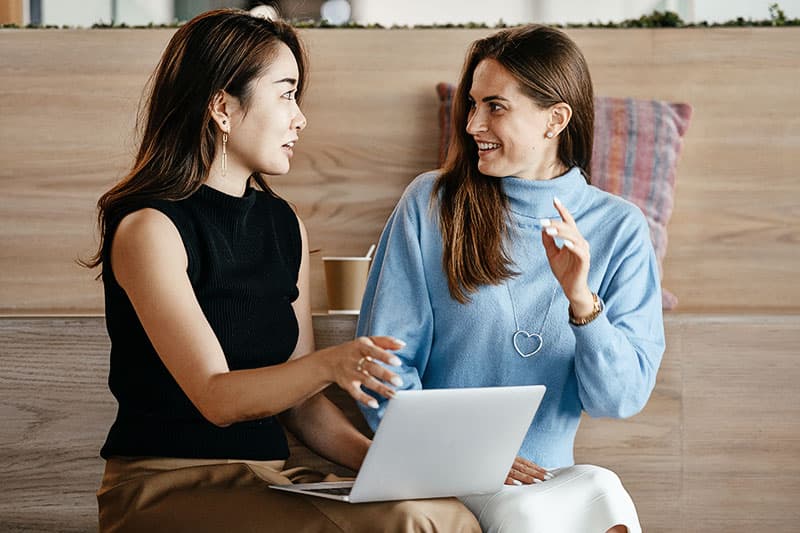 Two women talking and working on a laptop