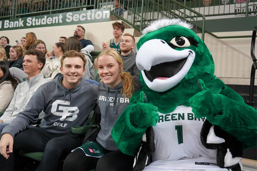 A group of people sitting in bleachers with a mascot Description automatically generated