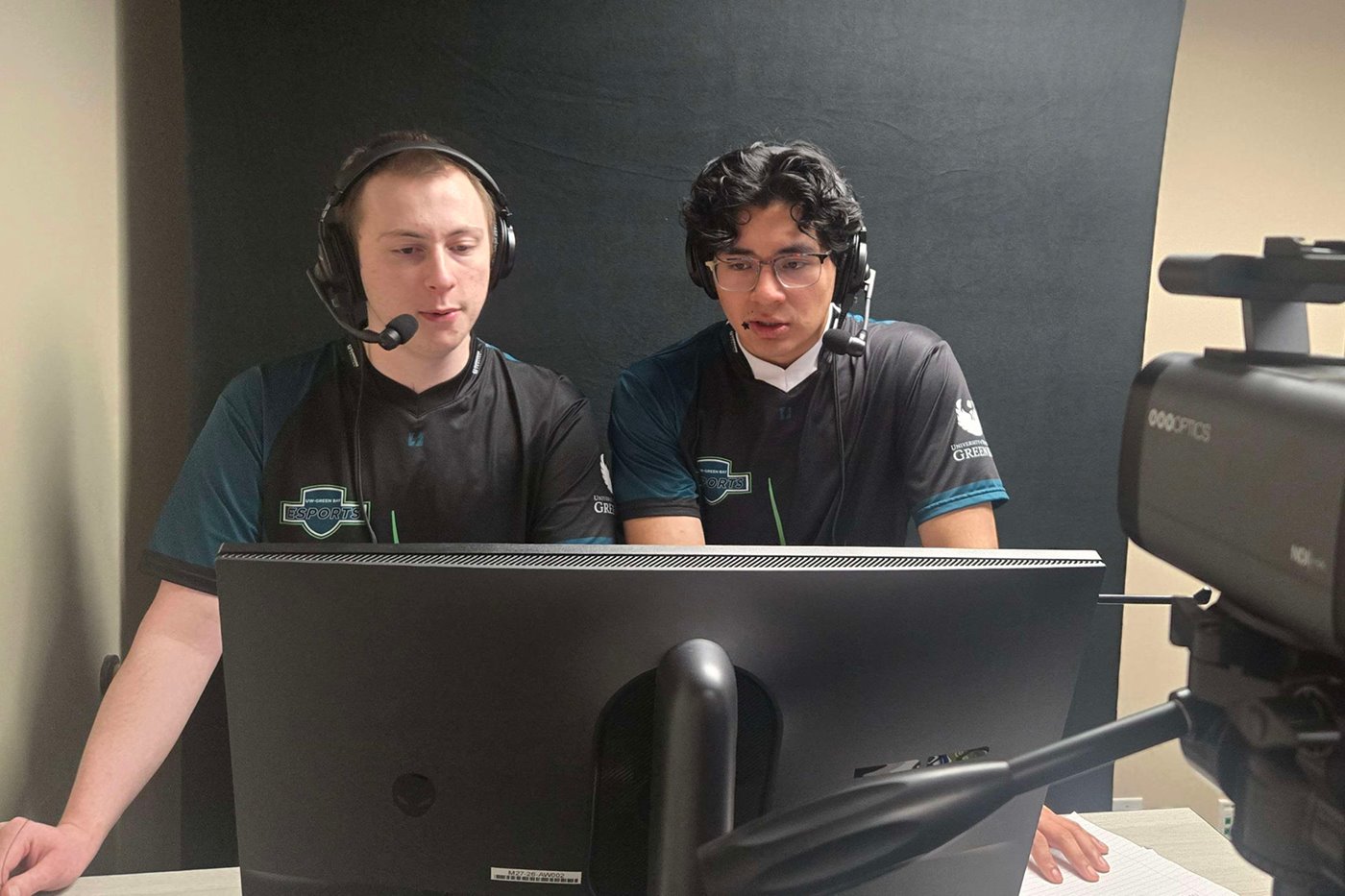 Two Esports team members with headseats look at a monitor.