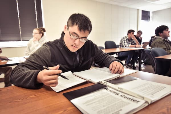 Asian male student works on paper in the writing center at UWGB