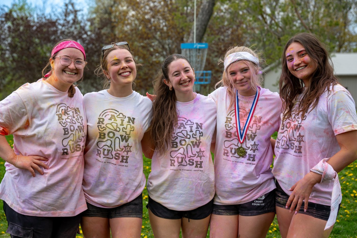 Five female students pose together, covered in bright colors after completing the Rainbow Rush 5K