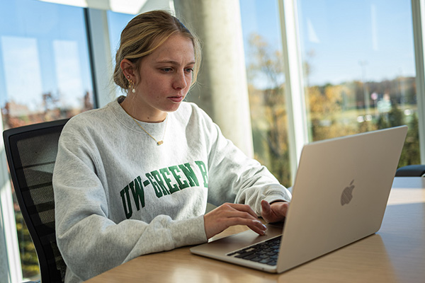 Female student in UW-Green Bay sweatshirt working on laptop