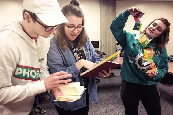 One male and two female students show off their creative writing porjects