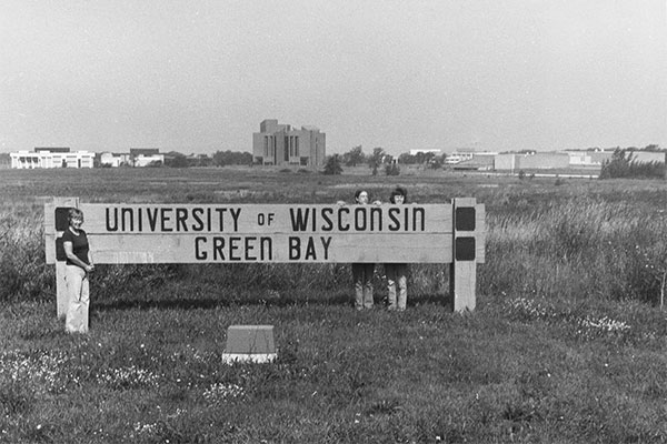 Early photo of students posed with a UW-Green Bay campus sign