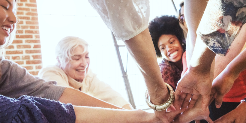 Diverse group of people putting their hands in a circle as seen from below.